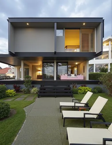 A modern two-story house with a minimalist design, featuring a large glass wall and sliding doors that open to reveal a cozy living area with a pink sofa. the house is surrounded by lush greenery and 