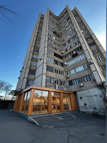 On the ground floor, instead of traditional blue iron outbuildings, there is a modern store characterized by glass windows and wooden elements.,a tall brown building sitting in the middle of a parking