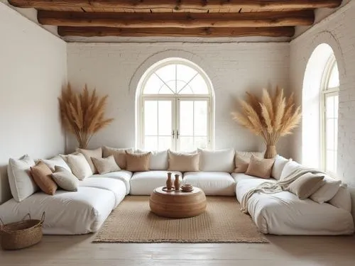 Bohemian-style living room with a soft and inviting aesthetic, featuring an oversized white sectional sofa filled with textured throw pillows in neutral and earthy tones. The walls are made of exposed