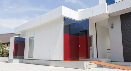 “Render exterior de un laboratorio ubicado en el garage de una casa. El diseño incluye paredes blancas, una pequeña cubierta roja sobre una puerta lateral con un acceso protegido, una ventana con marc