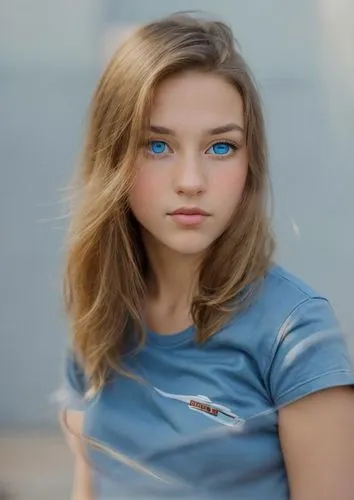 a close-up of a young caucasian girl with blue eyes and brown whiskers, dressed in a blue t-shirt, her reflection can be seen on her skin, she is looking directly at the camera, showing her time as ap