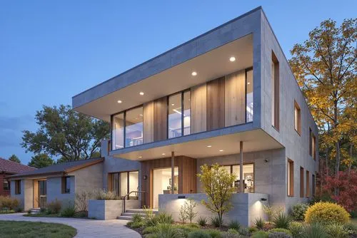 A modern two-story house with a minimalist design, featuring a combination of concrete and wood. the house is situated in a suburban area, with a clear blue sky and autumnal trees in the background. o
