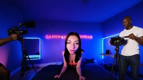 на стене весит неоновая вывеска надпись " casting ". видео студия ведётся видеосъёмка и лысый оператор с видеокамерой стоит спиной и снимает фильм. с краю на кровате трое мускулистых африканца,a woman