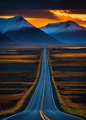 Two-lane road heading off into beautiful countryside of lake and mountains under a sunset sky. Colours of blue, orange and gold driving the Iceland ring road,eastern iceland,winding road,winding roads