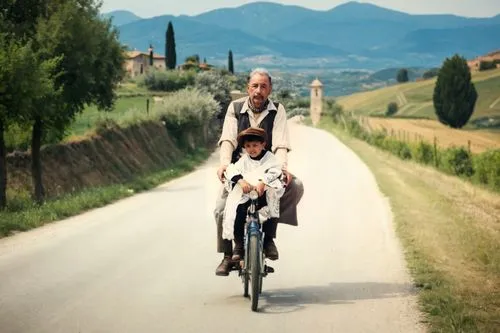 An old man with a child on a bicycle, with an Italian countryside road in the background,a man on a bike with his son in the back,bicycle ride,eroica,bicycle path,family motorcycle,woman bicycle,bicyc