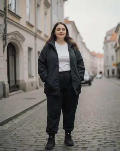 eine 23 jährige durchnittliche übergewichtige Estin in landestypischer Freizeitkleidung in einer mittelgroßen stadt in Estland. komplett angezogen,a woman wearing black is standing outside on the stre