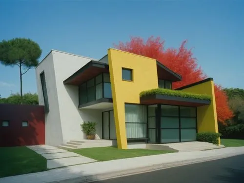 A front view of a red and white building in a neighborhood and a small garden of green grass. The house that is behind it is called a stepped home. It has four stories. It has a large tree in the midd