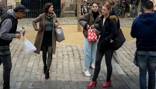 The woman on the left shields the two girls to the right of the center when the man—who appears to be an addict and is carrying a bag—tries to get too close to the girl in front. They call for the pol