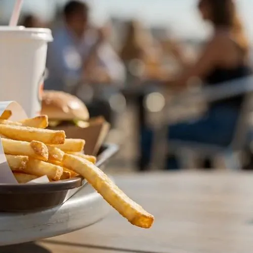 12-second comedy heist short for Western TikTok/Reels audiences, 16:9, no text, no logos, no subtitles.

0-2s: A summer cafe tray sits in close-up with one perfect fry hanging near the edge. A brazen 