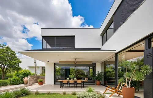 A modern, minimalist house with a minimalist design, featuring a white exterior with black louvered windows and sliding glass doors, set against a bright blue sky with fluffy white clouds. the house i