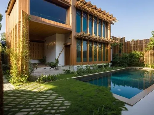 Una casa moderna de varios pisos hecha principalmente de madera clara y bambú, con extensos elementos de listones para dar sombra y atractivo estético. La casa está construida sobre pilotes en un exub