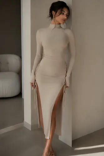 A young woman with a slim, hourglass figure, wearing a form-fitting light beige midi dress, high-neck design, long sleeves, dramatic thigh-high slits on both sides with delicate lace-up ribbon ties, e