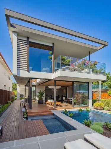 A modern two-story house with a contemporary design, featuring a large glass balcony on the upper level and a wooden deck on the lower level. the house is surrounded by a well-manicured lawn and a sma