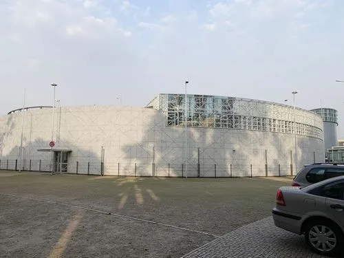 a car and building by a fence on the side of a road,synchrotron,gasometer,chancellery,sewage treatment plant,hangar,storage tank,grain storage,power station,cooling tower,concert venue,thermal power p
