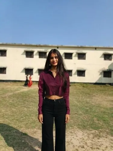 black shirt and crop ,a woman in a purple shirt and black pants posing for a picture,blurred background,a girl's smile,alumna,rani,college student,concrete background