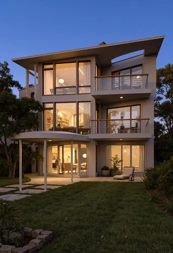 A modern, two-story house with a contemporary design, featuring large windows and a large balcony on the second floor. the house is situated on a hillside, with a well-manicured lawn and a stone pathw