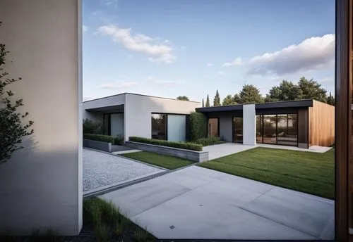Perspectiva exterior de una casa moderna de un solo nivel, con volúmenes geométricos minimalistas y líneas limpias. La fachada combina concreto blanco con detalles en madera y vidrio, integrando ampli
