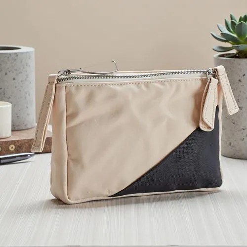 A contemporary zipper pouch with a unique geometric design, made of smooth, structured fabric in contrasting tones of beige and charcoal gray. The zipper is polished chrome with a chunky triangular pu