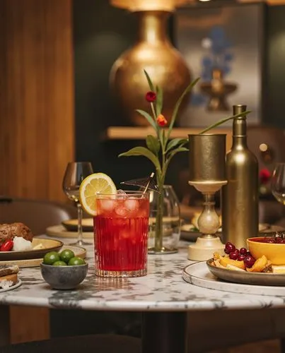 A luxurious table setting featuring a modern glass tumbler filled with a vibrant red cocktail garnished with a lime slice and a small cocktail umbrella, surrounded by elegant dishware, fresh berries,