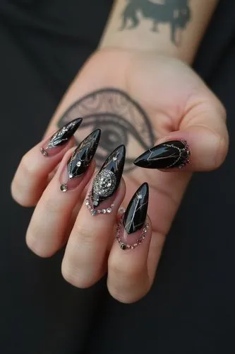 Nils Design, hallowen nails,
A mix of gothic and alternative nails with bold black stiletto designs, featuring an all-seeing eye motif, set against a dark grey background. The manicured hands display 