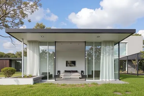 A modern, minimalist house with a minimalist design, featuring a large glass walled entrance and a black metal roof. the house is situated on a grassy area, with a clear blue sky and fluffy white clou