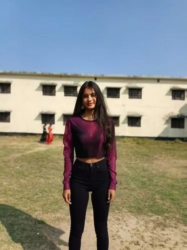 black shirt and crop ,a woman in a purple shirt and black pants posing for a picture,blurred background,a girl's smile,alumna,rani,college student,concrete background