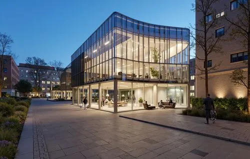 a large, glass covered building sits among several apartment buildings,broadgate,freshfields,goldsmiths,aldermanbury,mvrdv,brindleyplace,music conservatory,glass facade,chipperfield,rikshospitalet