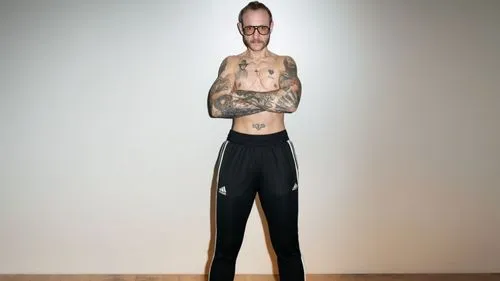 спортивные чёрные штаны Адидас,a man standing in front of a white wall,elongated,elongate,legman,tall man,long son,slender,skinniest,lanky,a wax dummy,standing man,pants,stilt,necks,anorexic,slim,tran