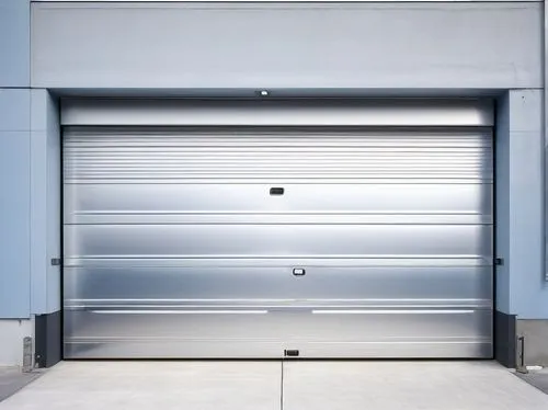Modern commercial garage door, sleek metallic finish, automatic sliding system, LED lights underneath, polished concrete floor, urban industrial setting, daytime, clear blue sky, partial view of citys