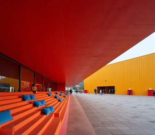 Indoor view of a red staircase, with orange carpet and matching blue cushions in the foreground, partially visible behind the stairs, arranged in a row from left to right, showing the interior of the 