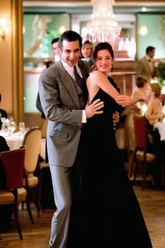A man in a suit and a woman in an evening gown are dancing in a fancy restaurant.,man and woman in dress clothes posing for the camera,argentinian tango,milonga,dancing couple,waltzing,tango argentino