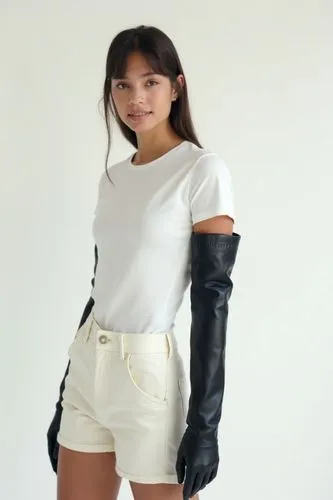 Her entire outfit is white: a basic fitted t-shirt, soft wool shorts, and a minimalist white belt. On her arms and legs, however, shiny black leather explodes — the gloves go to the shoulders, tight a