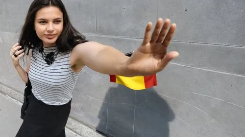 A girl reaches out with an outstretched arm for a German flag in front of a neutral gray concrete facade.,there is a woman with her arm raised,woman holding gun,woman pointing,sprint woman,pointing wo
