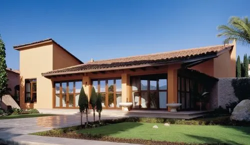 Una casa de estilo mediterráneo contemporáneo, con techos inclinados cubiertos de tejas de barro rojo tradicionales, aportando un carácter cálido y artesanal. La fachada principal incluye amplios vent