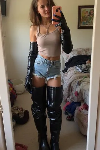 A young 18-year-old woman takes an amateur mirror selfie, shared as an Instagram story, showcasing her personal style. She wears eye-catching accessories that stand out against her simple, everyday ou