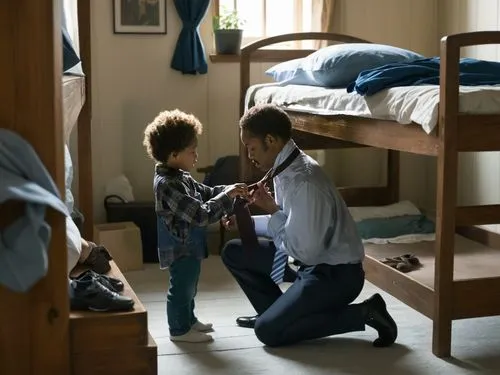 A man crouches down and a small child is helping him tie his tie. In the background there is a wooden bunk bed in a room,a man kneeling on the floor with a young child,lubezki,wallander,photographing 