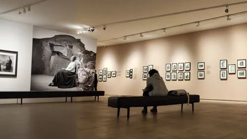 the sitting woman is looking at a black and white photograph in a museum ,a man sitting on a bench in an art gallery,fotomuseum,gallery,galleries,exhibitions,art gallery,universal exhibition of paris,