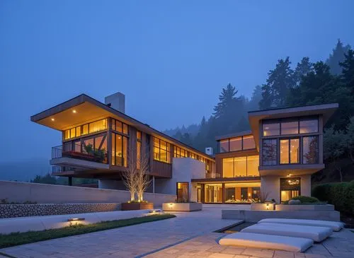 A photo-realistic shoot from the side about a modern, minimalist house at night with a mountain view in the background. the image also shows the exterior of the house, which is a two-story building wi