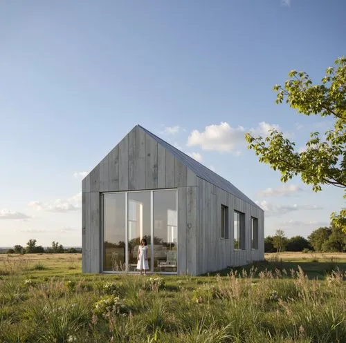 At the Countryside Meadow,the woman stands in front of the tiny house,inverted cottage,timber house,passivhaus,cubic house,frame house,danish house,summer house,cube house,frisian house,wooden house,e