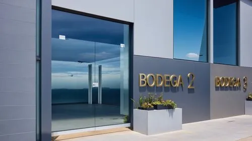 “Vista detallada de la entrada de la ‘Bodega 2’ en un complejo industrial moderno. La entrada cuenta con una puerta doble de cristal con tiradores metálicos minimalistas, que permite visibilidad hacia