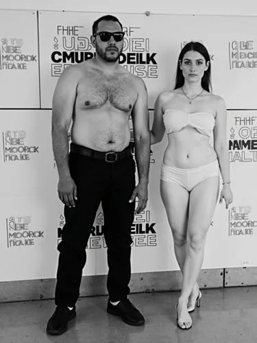 Black and white couple in front of a brand wall at a film festival.,a man and a woman standing together for the camera,grek,mobster couple,stand models,greeks,chippendales,stav,objectification,cukor,m