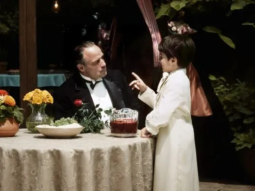 Elderly man and child in gowns at table with outdoor garden in the background,a boy and an older man at a table,tea ceremony,autochrome,waiter,tableside,communion,video scene,headwaiter,godfather,cher