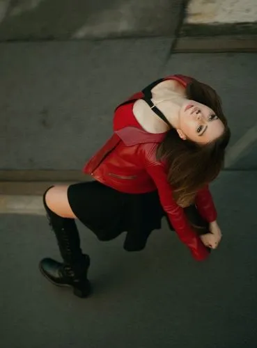 A conceptual art of a beautiful caucasian young woman, staning in a street. She has long brown hair, is wearing a red leather jacket and a black minidress whit a neckline and longblack loots . She has