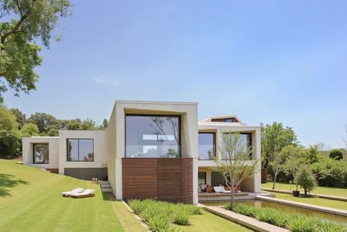 A modern minimalist house with large square glass windows, beige concrete walls, and horizontal wooden slats, positioned in an open green lawn under a clear blue sky.,a very modern, simple house near 