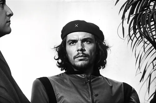 A striking black-and-white portrait of a revolutionary figure with intense eyes and a determined expression, gazing slightly upward as if envisioning the future. He wears a beret adorned with a single