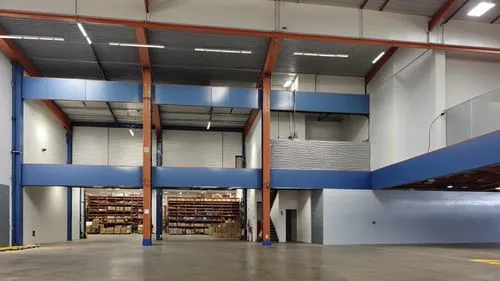 “Vista interior de una bodega industrial moderna, caracterizada por amplios espacios abiertos, estructuras metálicas en color negro y columnas de madera que soportan entrepisos. Las paredes en tonos g