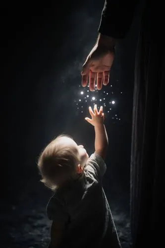 Close-up: A small child's hand reaches up from below for an adult's hand, set against a dark background with a mystical atmosphere.,someone reaching up for a lite - up fireworkshopper,child's hand,pho