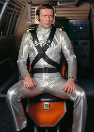 1970’s man sat wearing a silver metallic flight suit with a bulging crotch in a futuristic cockpit.,yuri gagarin,kryten,gorshin,dobrien,kuenzer,ekornes,baumgartner,emperor of space,hopkirk,space suit,