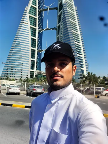 a man wearing a baseball cap stands in front of a building,jumeirah beach hotel,burj al arab,habtoor,dubay,largest hotel in dubai,jumeirah beach