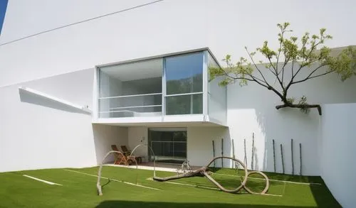 UNA CASA  ESTILO MINIMALISTA CON UN MURO DECORADO CON UNA JARDIENRA CON PLANTAS DE FORMIO, UN GRAN ARBOL SALE DE LA BARDE QUE LIMITA LA CASA, UNA GRAN PUERTA DE MADERA DE CEDRO DE ACCESO, Y EN LA PLAN